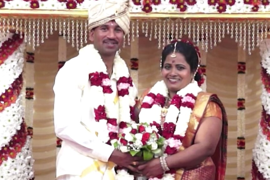 Two people dressed in wedding attire smiling.