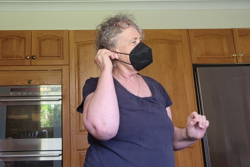 A woman wearing a black N95 face mask in a kitchen with wooden cupboards