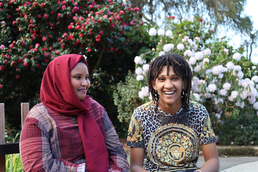 A woman sits next to a young man, smiling at him while he smiles at the camera