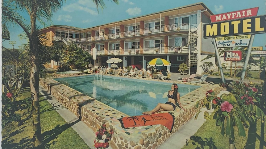 Postcard of old three storey motel with palm tree over the pool and a woman sunbathing by the unfenced pool