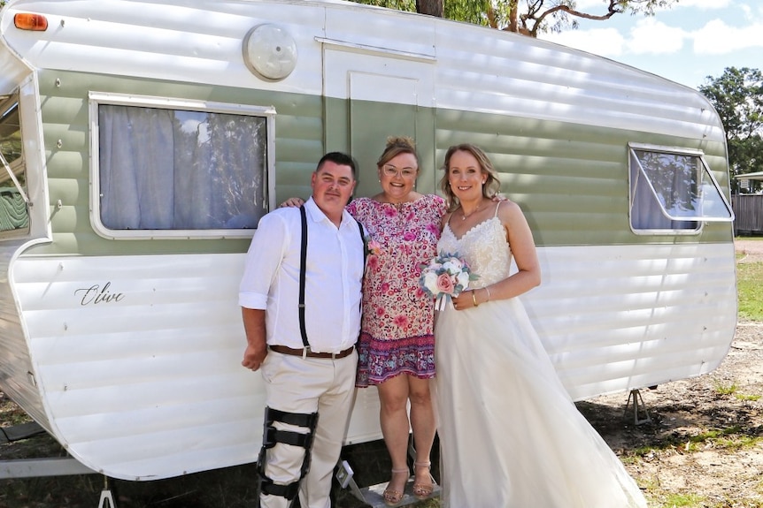 Julie Dominish poses with a couple on their wedding day in front of Olive the caravan.