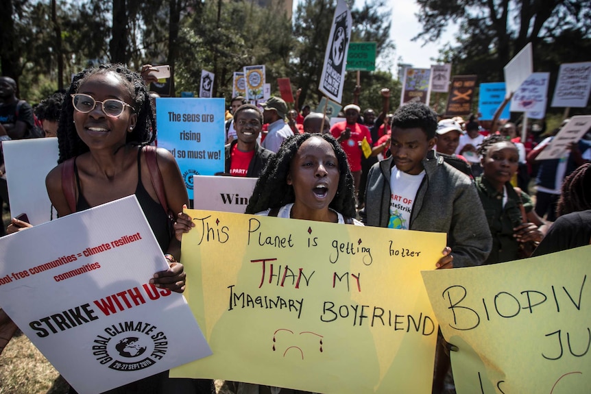 Three teenage girls walk through the streets of Nairobi carrying placards.