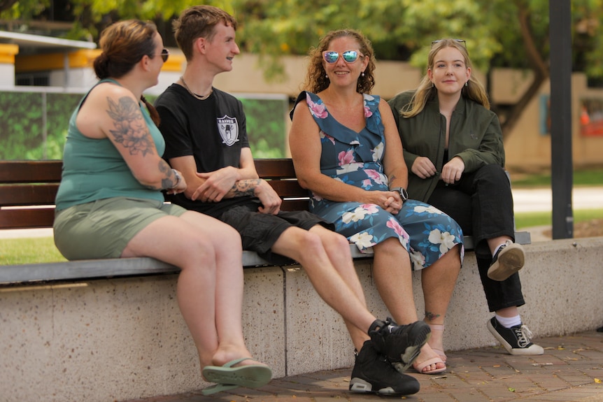 Four people sitting on a park bench.