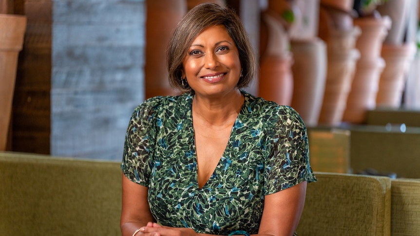 Indira Naidoo, sitting at a table with warm-toned earthenware sculptures in the background.