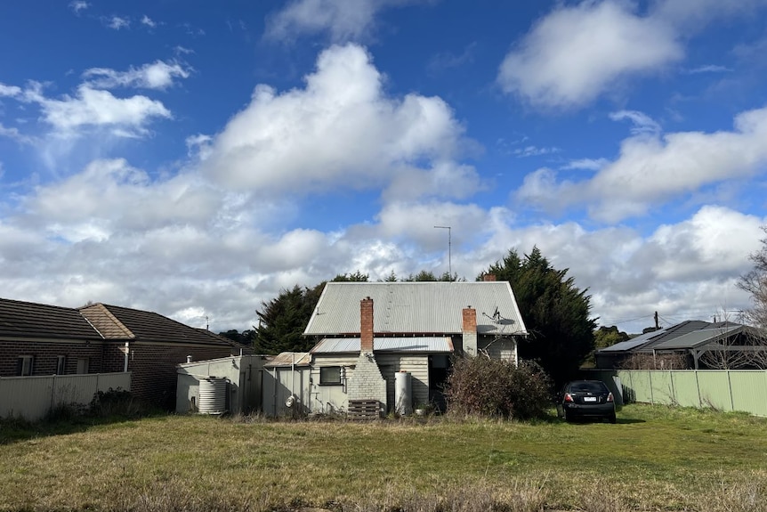 A weatherboard home in a big grassy yard with the blue sky and clouds. 