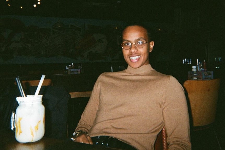 Yusuf Liban sits at a restaurant table, smiling at the camera. 