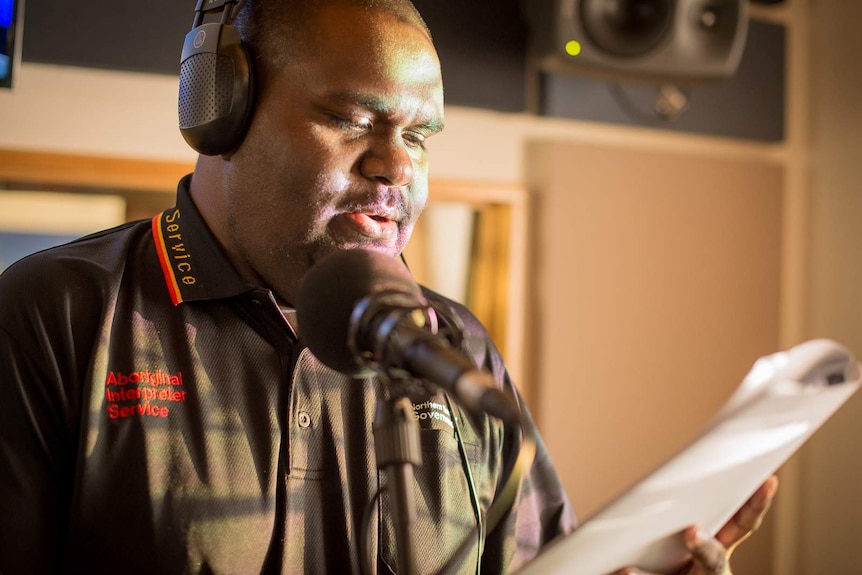 An Indigenous man reads from a script as he translates the news into language inside a radio broadcasting studio.