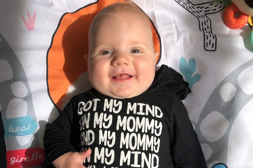 A baby smiles at the camera as he lies on his back.