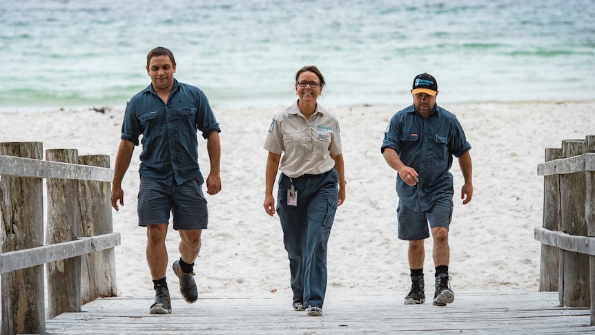 Three people walk toward a beach.