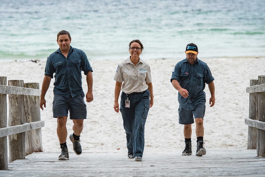 Three people walk toward a beach.