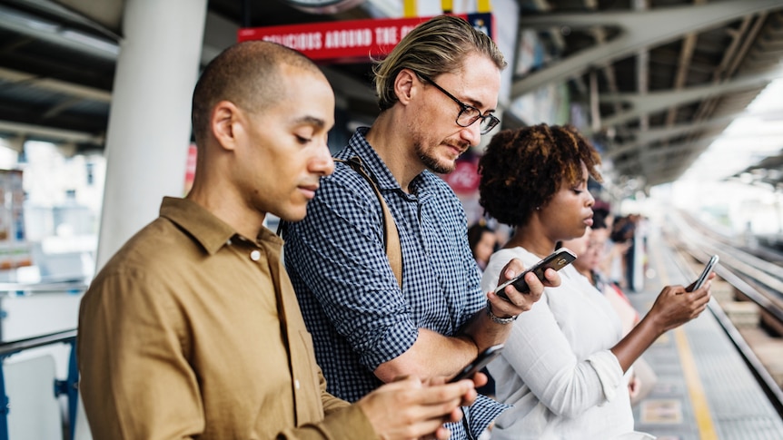 Commuters waiting on a train station looking at their phones.