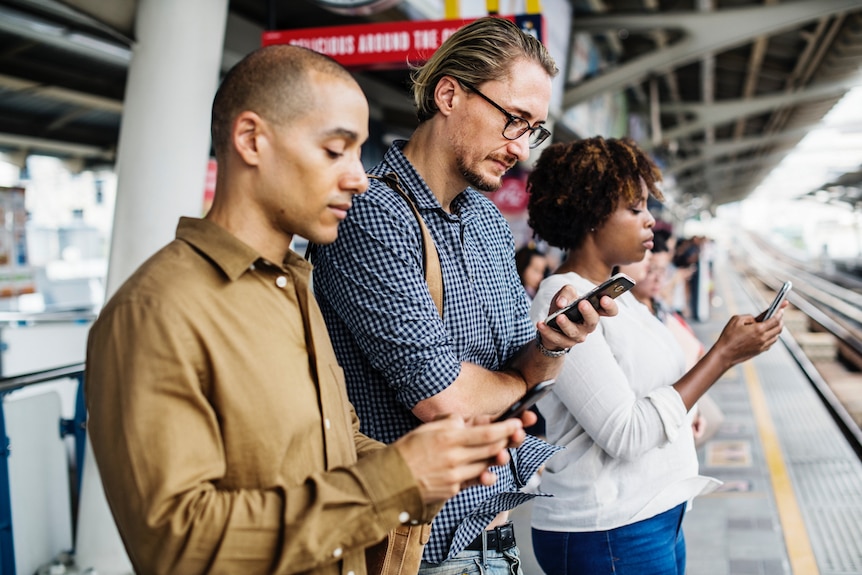 Commuters waiting on a train station looking at their phones.