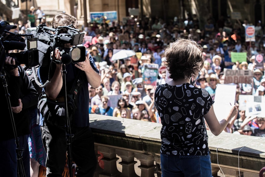 young girl speaking to audience with TV cameras filming her