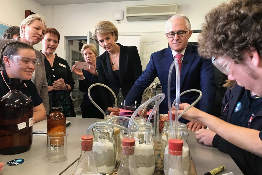 Prime Minister Malcolm Turnbull stands next to Michaelia Cash watching high school students carry out a science experiment.