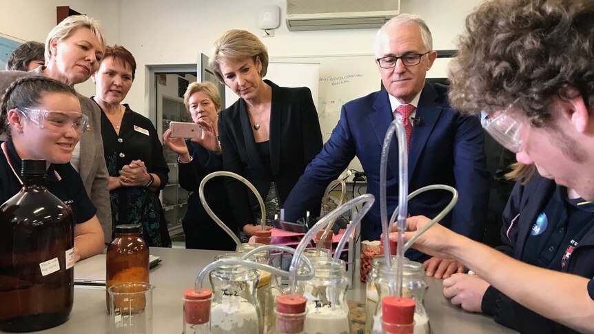 Prime Minister Malcolm Turnbull stands next to Michaelia Cash watching high school students carry out a science experiment.
