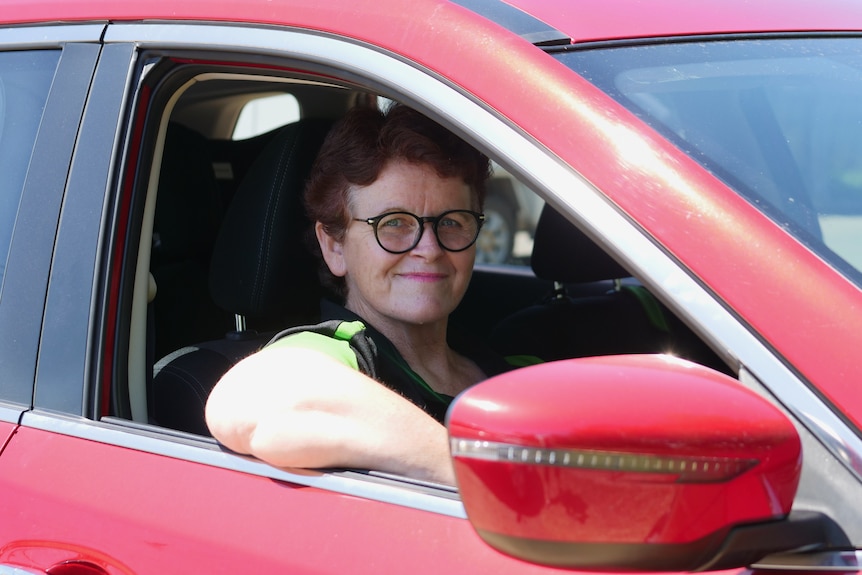 A woman sitting in the driver's seat of a red car, smiling.