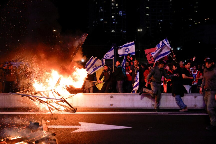 A barricade is on fire as protesters wave Israeli flags behind it