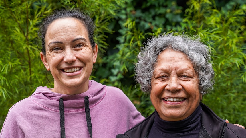 Two women stand in front of a bush smiling.