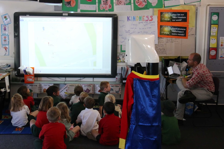 A mobile robot stands behind a class of kids.