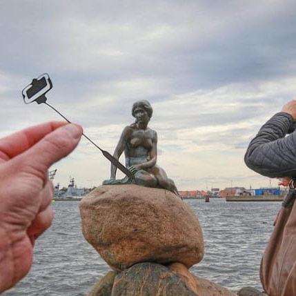 A photo of the Little Mermaid statue in Copenhagen with a selfie stick cut