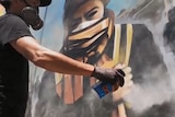 A man wearing breathing protection spraypaints a mural on a wall.