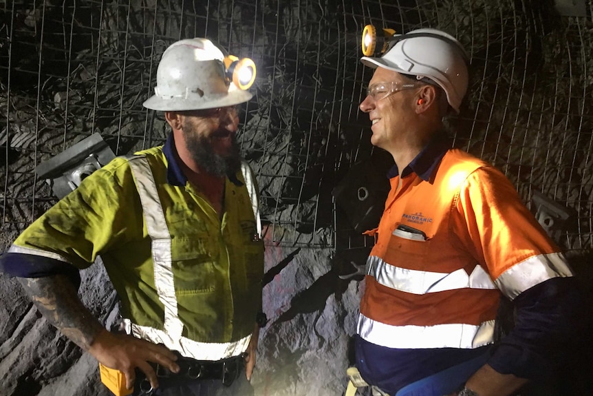 Mid shot of two men talking in underground mine wearing high vis clothing and hard hats