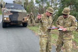 Uniformed army personnel discuss plans while standing near a defence truck