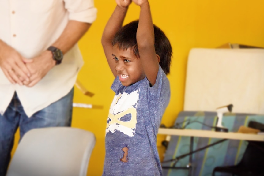 Young Aboriginal kid participates in a drama workshop wearing a pruple shirt with yellow wall behind