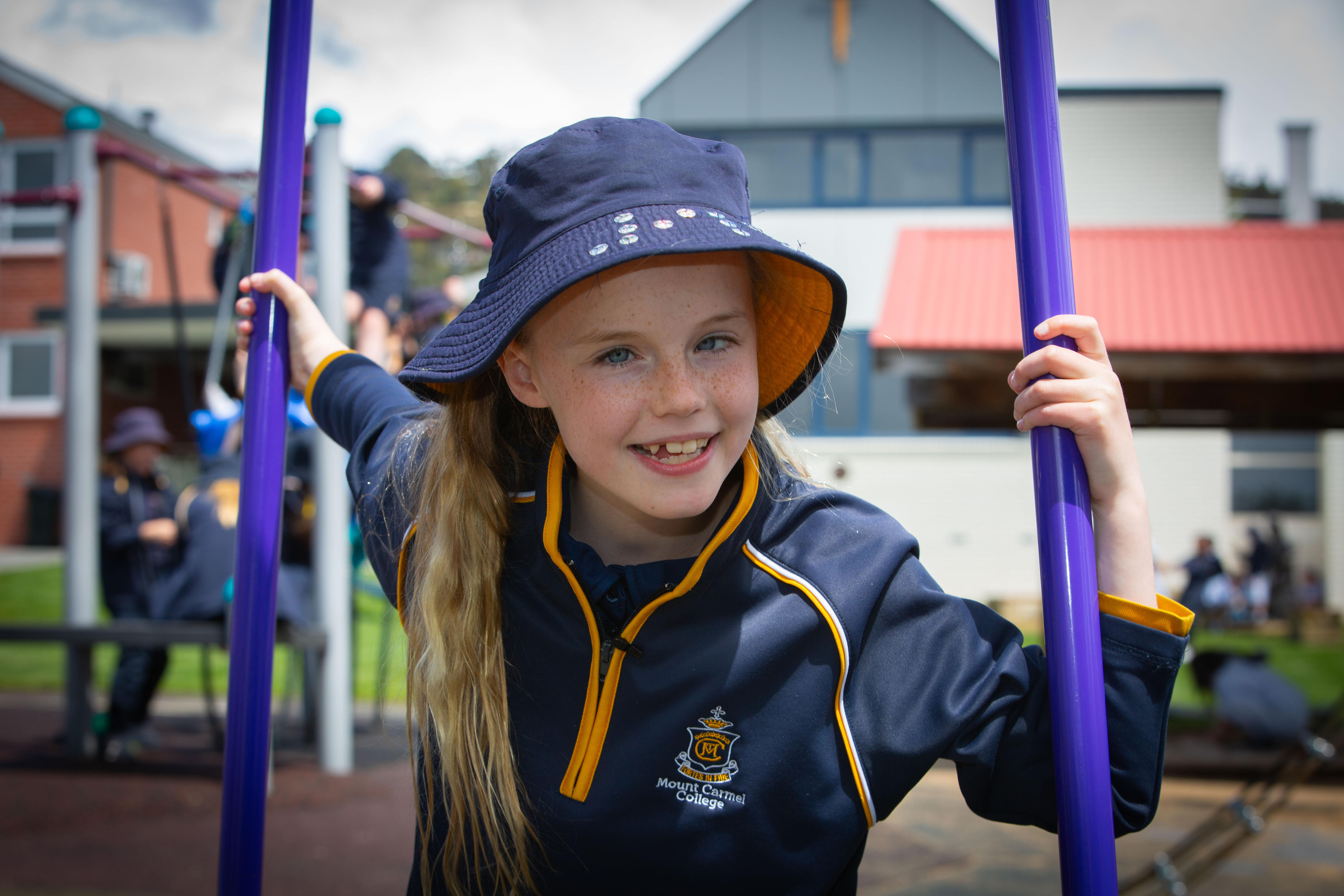 Una niña con sombrero de pescador se agarra a postes verticales mientras juega en el recreo.