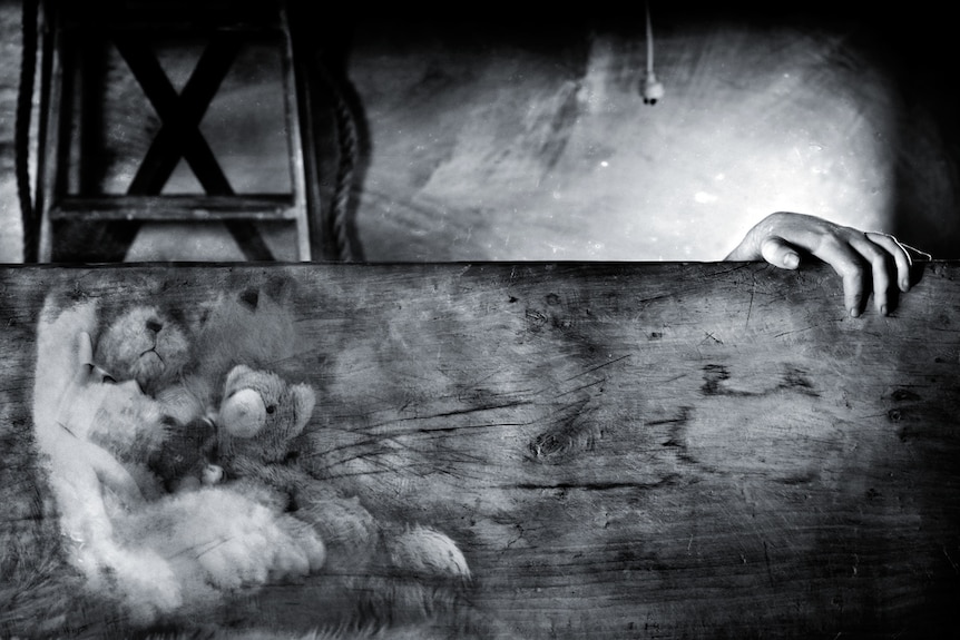 An artistic photograph shows a hand on a piece of wood with the image of a teddy bear on it.