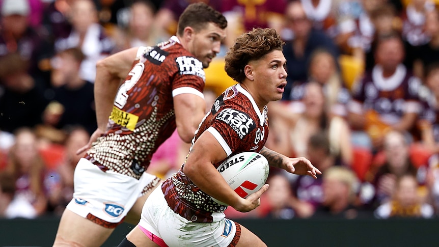 NRL player Reece Walsh running with the ball, with teammate Corey Oates on his left in support