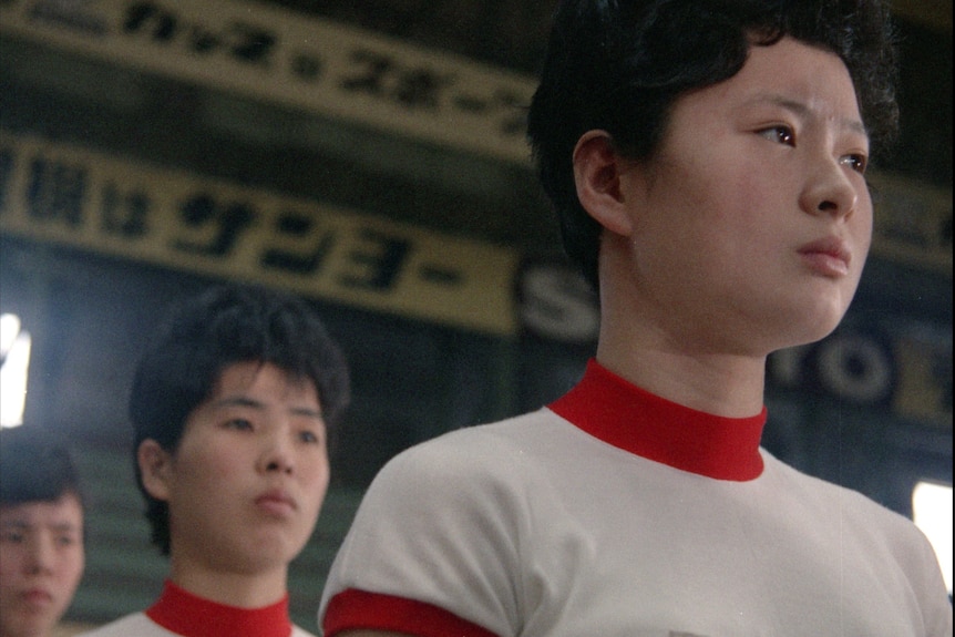 Two young Japanese women , members of the 1964 Volleyball team, in sports uniform, looking serious.