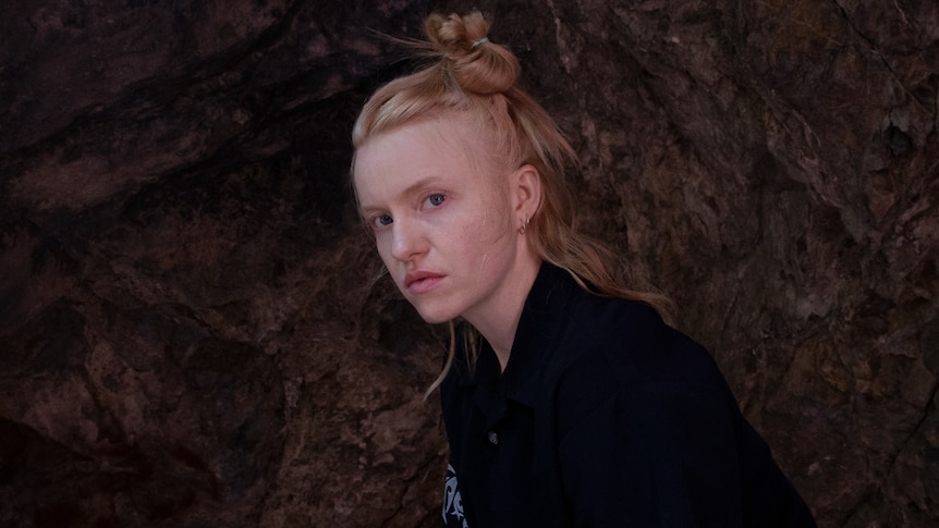 Press shot of KUČKA, dressed in black against stone wall