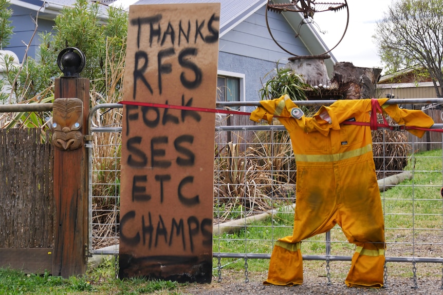 A board with a spray-painted message of thanks to emergency services strapped to a fence next to a pair of overalls.
