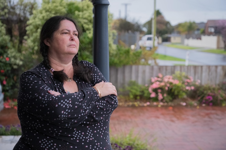 A woman holds a mug and looks mournfully out the kitchen window.