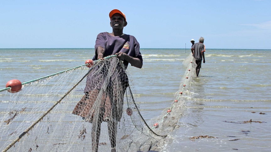 a man pulling a net out to sea with two other men behind.