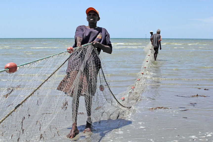 a man pulling a net out to sea with two other men behind.