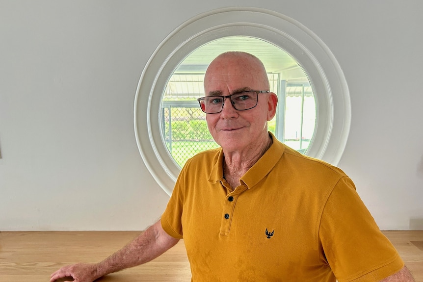 A smiling, bald man standing in front of round window.