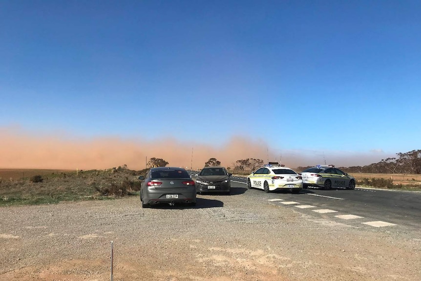 Police vehicles block a rural highway, with dust visible.