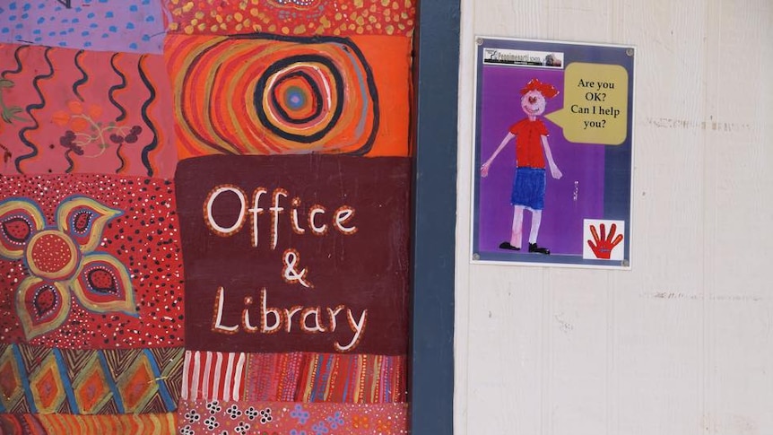 A sign reading "office and library" with Indigenous artwork in a school.