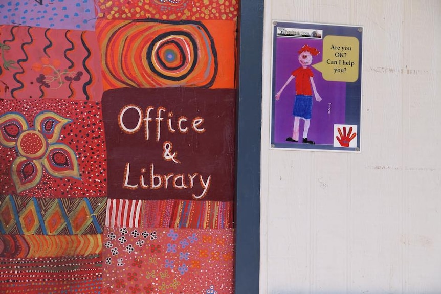 A sign reading "office and library" with Indigenous artwork in a school.