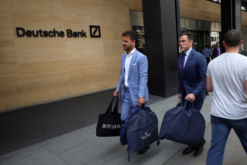 Two men in suits carrying bags in front of the Deutsche Bank in London.