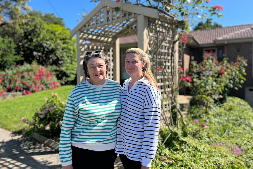 Two women wearing stripy jumpers smiling and posing in front of a garden.