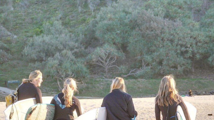 A group of girls walk down a beach holding their surfboards
