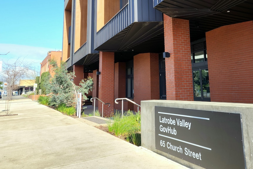 A sign that says "a kinder cup" in front of a modern black and orange building.