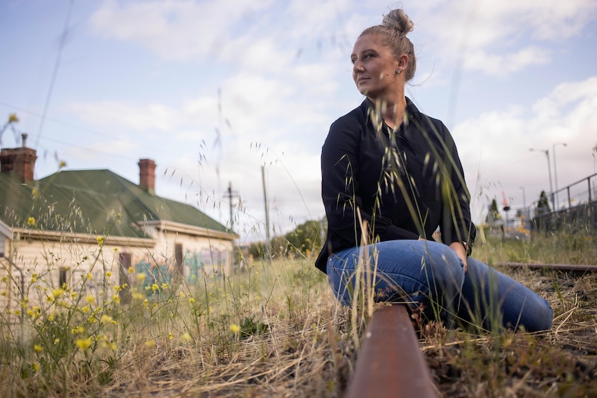 Woman in jeans and a jacket sitting in a field. 