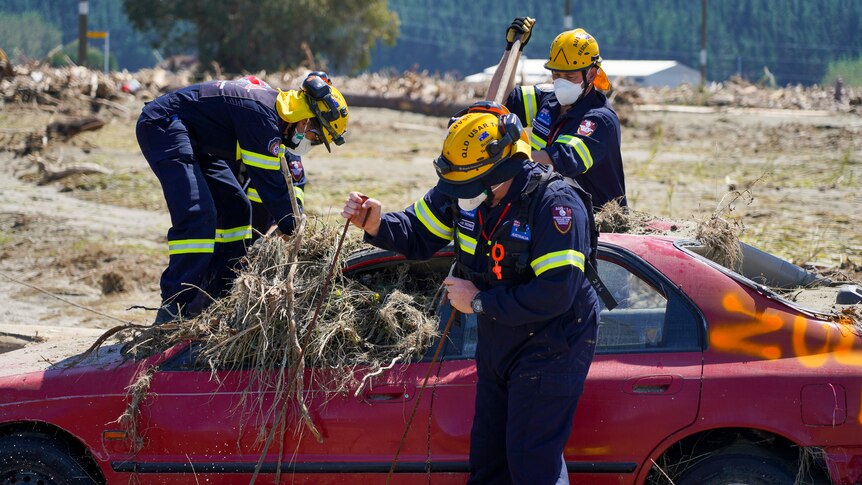 Three firefighters try to search a maroon car that is full of mud and grass