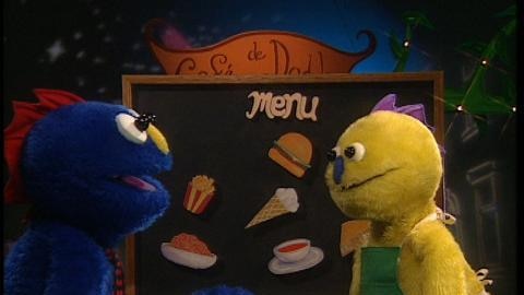 Blue and yellow puppet figures stand in front of menu board