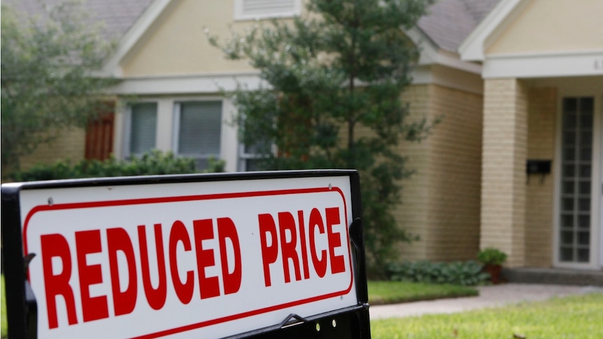 A house for sale, with a "Reduced price" sign on the front lawn.