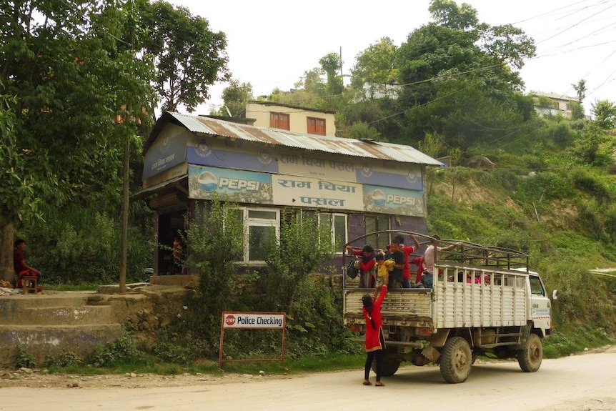 Nepali girls climb aboard a truck in front of a dilapidated building